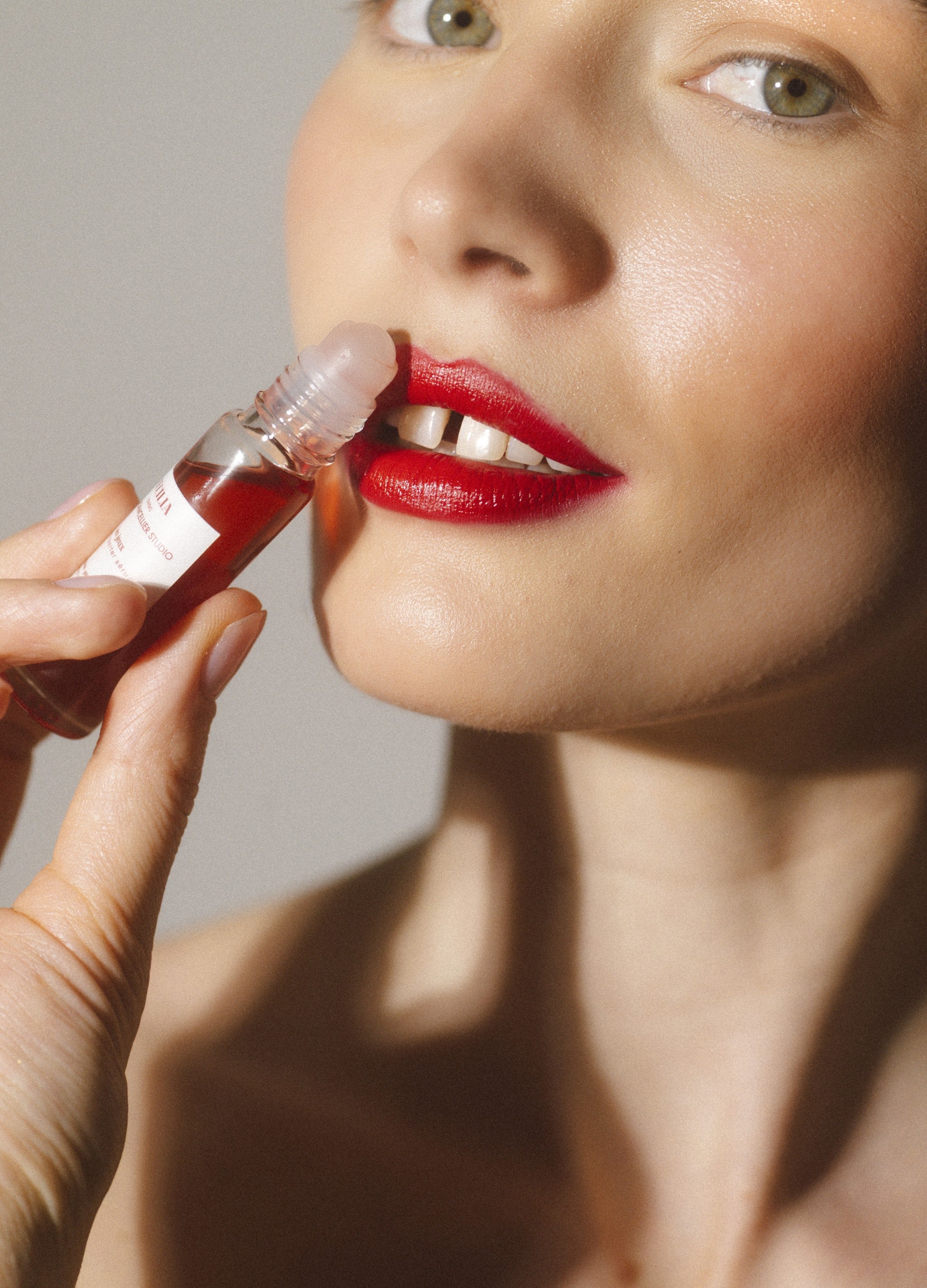 Close-up of a woman applying red lipstick with a small tube.