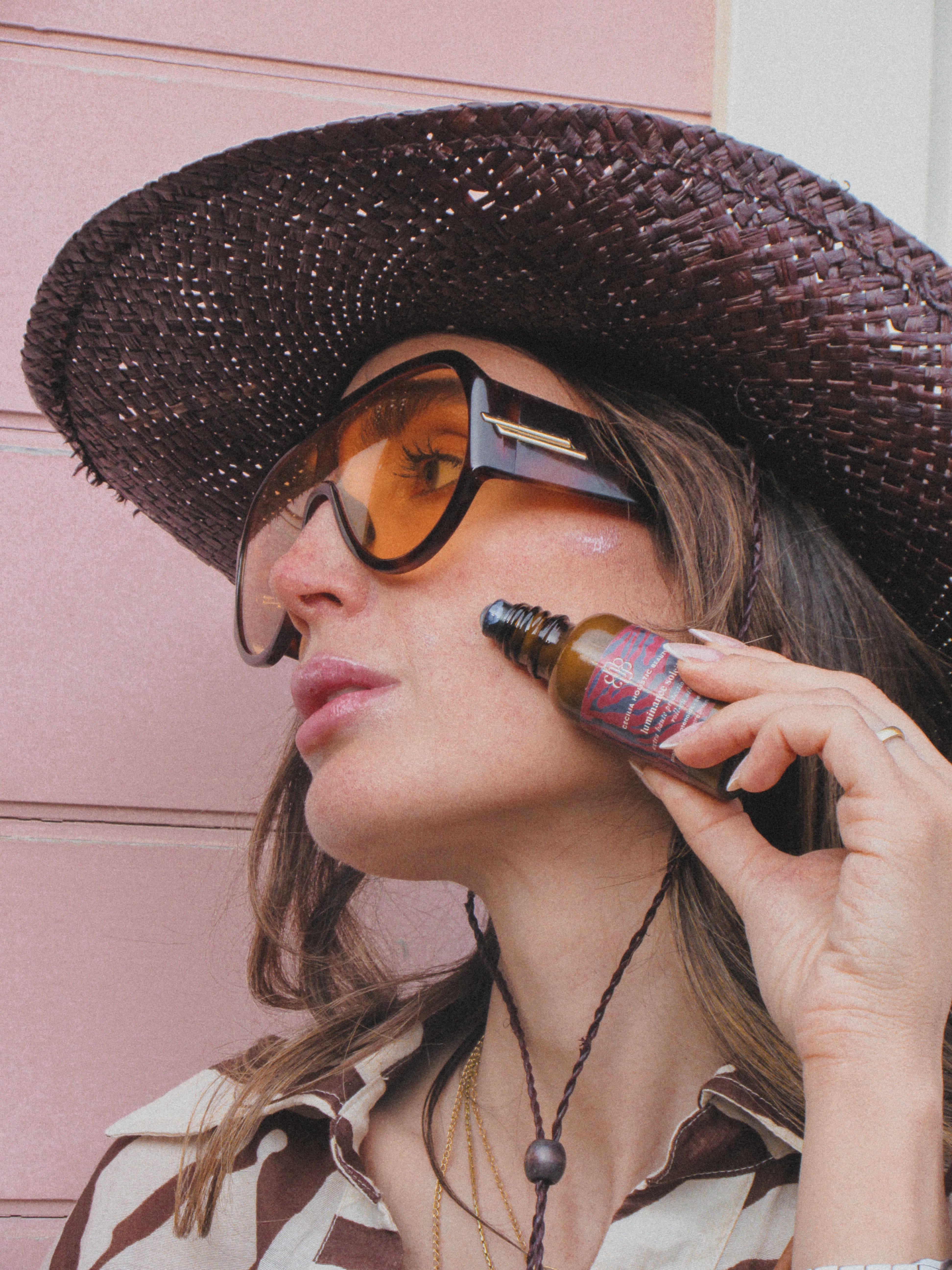 Woman applying sunscreen with a bottle against a pink wall